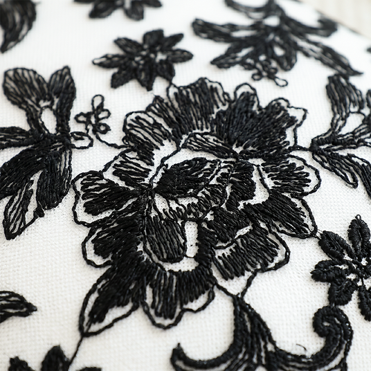 close up of black embroidered flower on white pillow