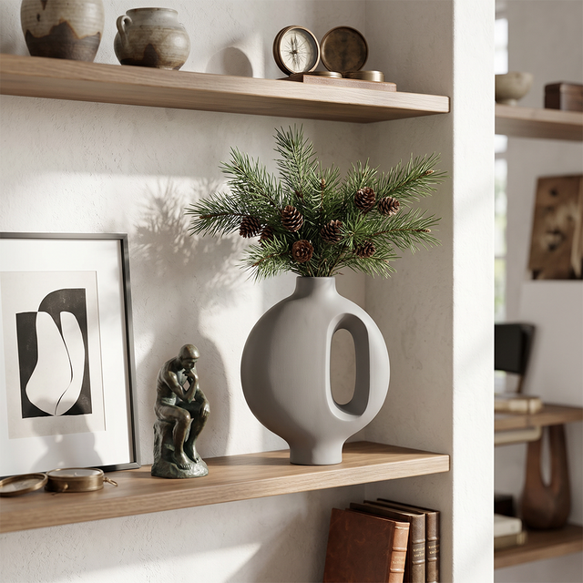 grey vase with pine branches on wooden shelf