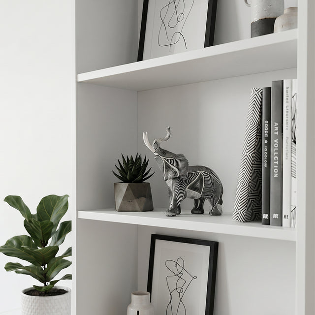 Carved elephant statue inside white open bookshelf
