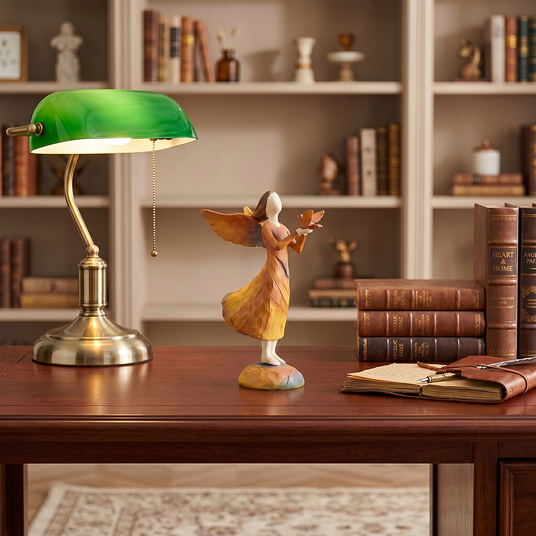 angel holding bird figurine on wooden desk with lamp