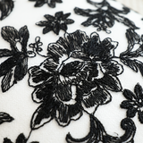close up of black embroidered flower on white pillow