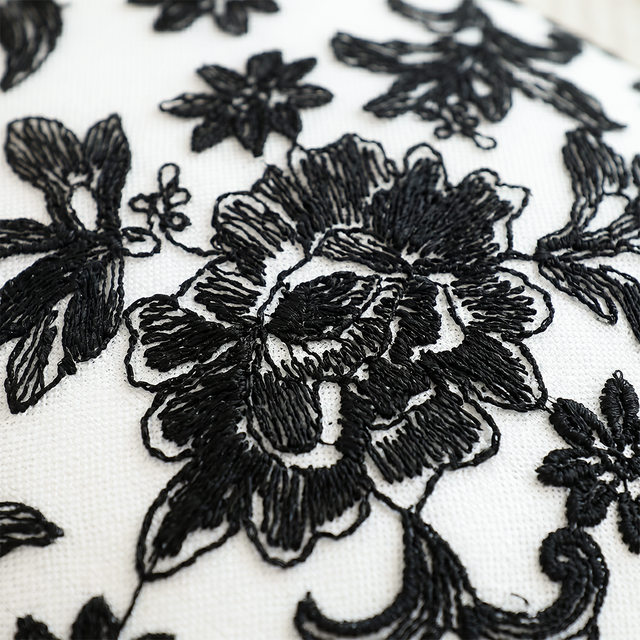 close up of black embroidered flower on white pillow