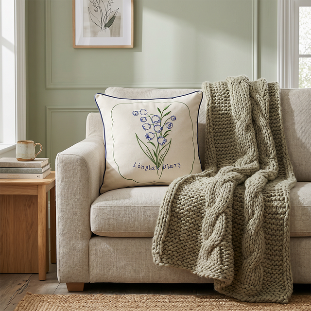 embroidered lily pillow on beige sofa with chunky blanket