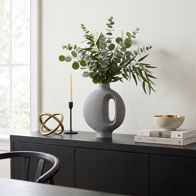 grey vase with eucalyptus on dark sideboard near window