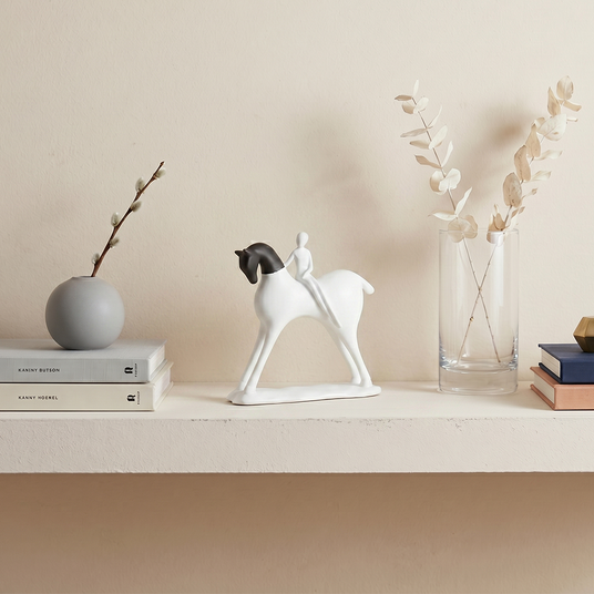 horse and rider sculpture on beige shelf with vases