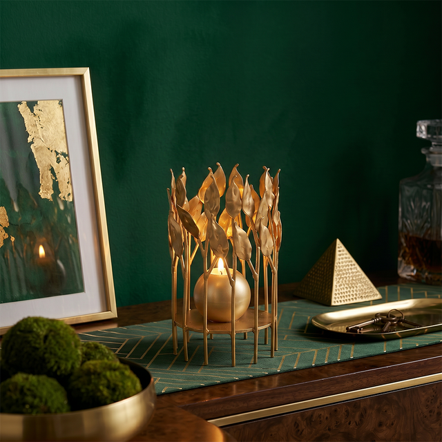 lit gold leaf candle holder on dark green cabinet