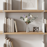 silver vase with flowers on light wood shelf