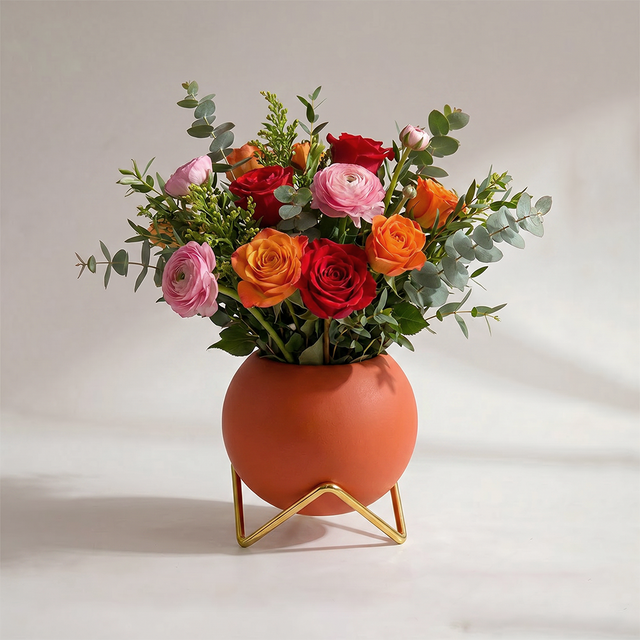 terracotta spherical vase on gold stand with flowers