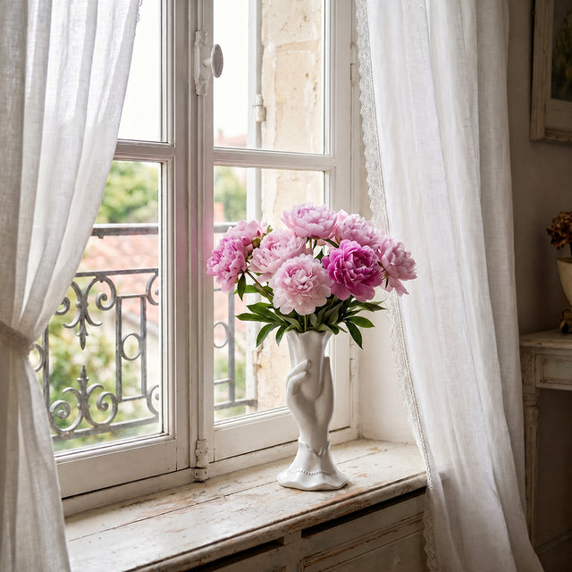 white hand vase with pink flowers on windowsill
